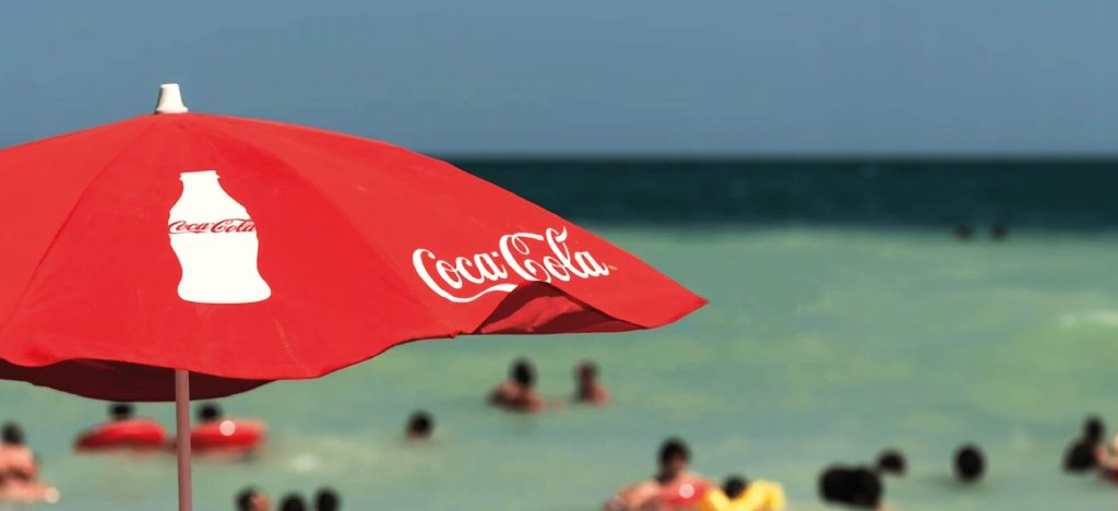 un paraguas personalizado con el logo de Coca-Cola en la playa