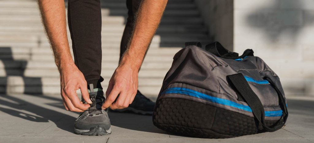 hombre atándose las agujetas junto a un bolso deportivo