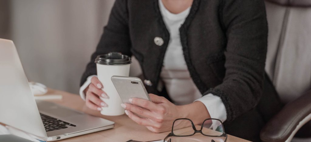 persona con portátil, un vaso termico con café y su movil