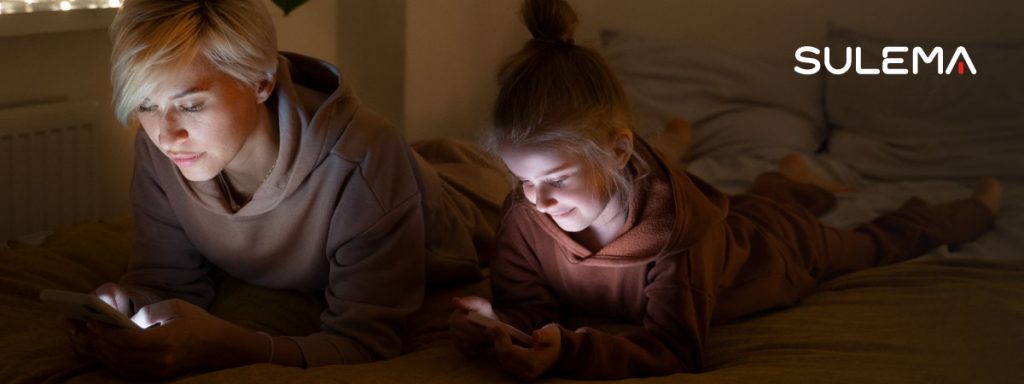 una madre e hija con su móvil recostadas en la cama, desconectadas de la vida real