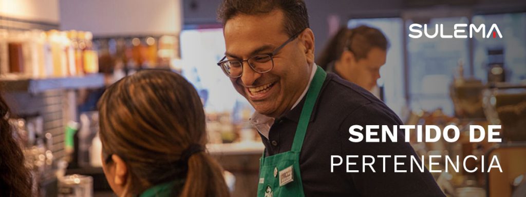 Texto: "Sentido de pertenencia", se ve a un empleado de Starbucks sonriendo con un delantal personalizado