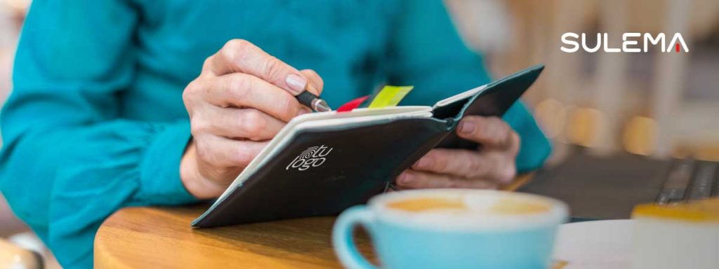 Persona escribiendo en una libreta corporativa personalizada